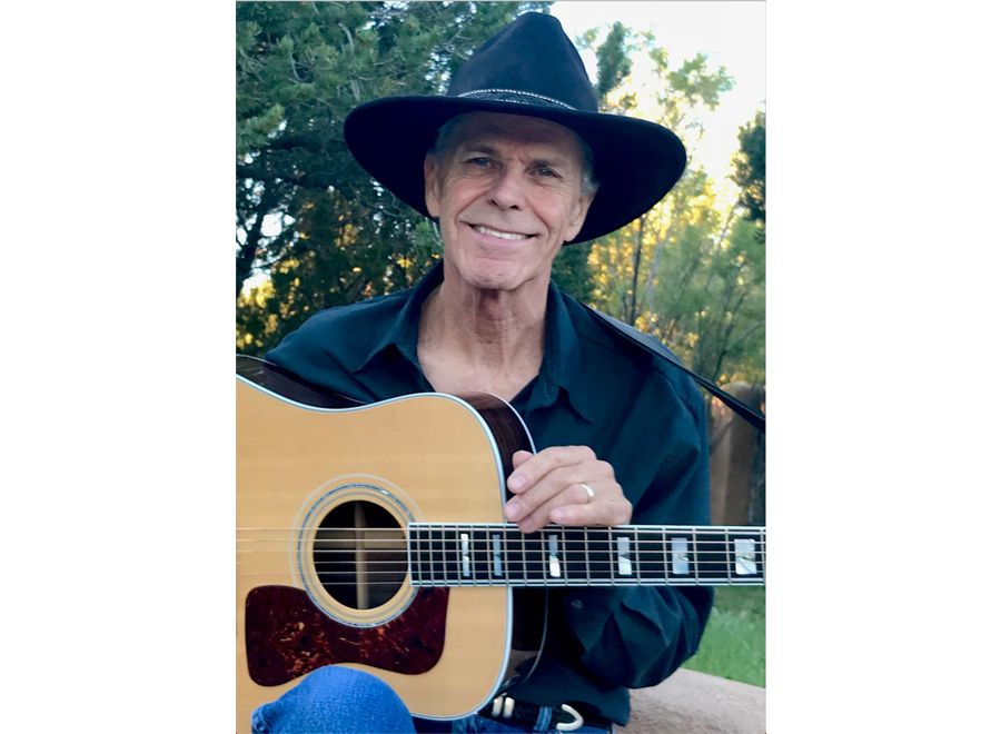 A Man Wearing A Hat And Holding A Guitar
