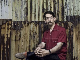 Fred Hersch Sitting On A Bench In Front Of A Curtain